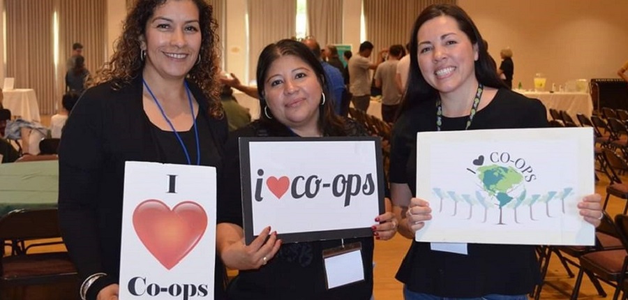 Three women holding signs that promote co-ops